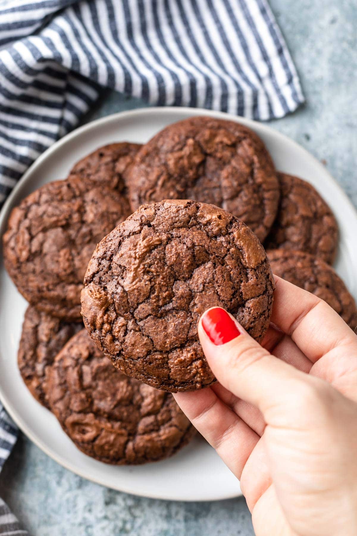 close up of hand holding a brownie mix cookie, bowl of cookies in background