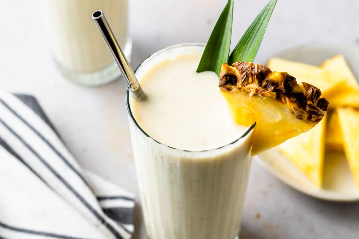 pina colada smoothie with pineapple slices on a plate in the background