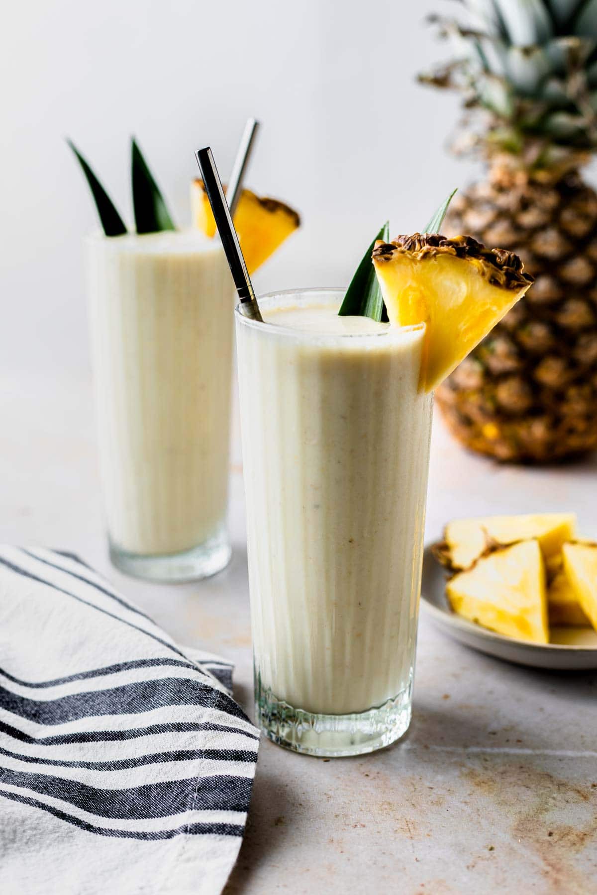 two pina colada smoothies garnished with pineapple wedges with a fresh pineapple in the background