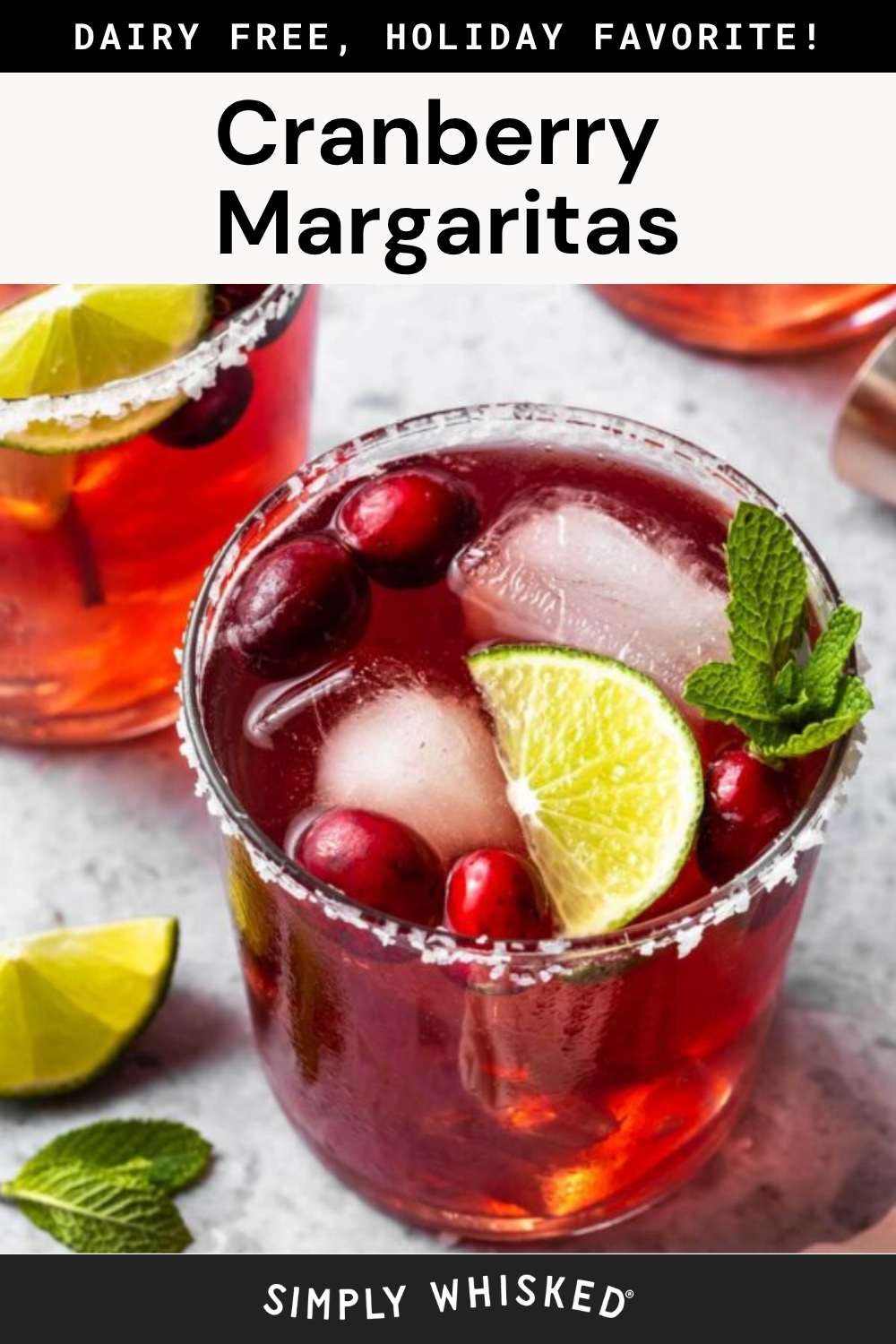 A glass of vibrant cranberry margarita, one of two refreshing cranberry margaritas garnished with cranberries, a lime wedge, and fresh mint, sits with ice cubes on a light surface beside another similar drink.