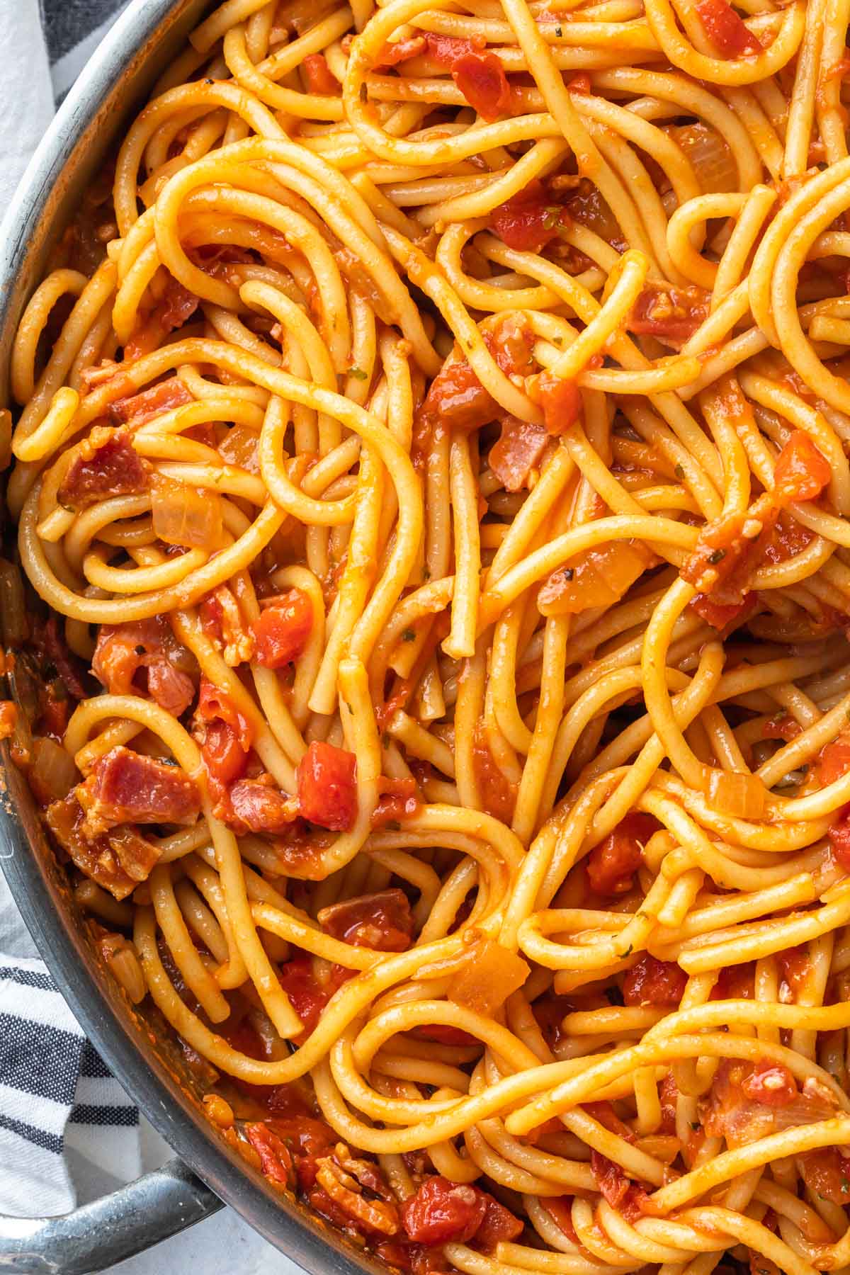 A close up of large skillet full of bucatini with sweet onion and pancetta sauce. 