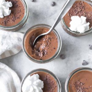 homemade chocolate pudding in small mason jars topped with chocolate shavings and dairy free whipped cream on a gray surface