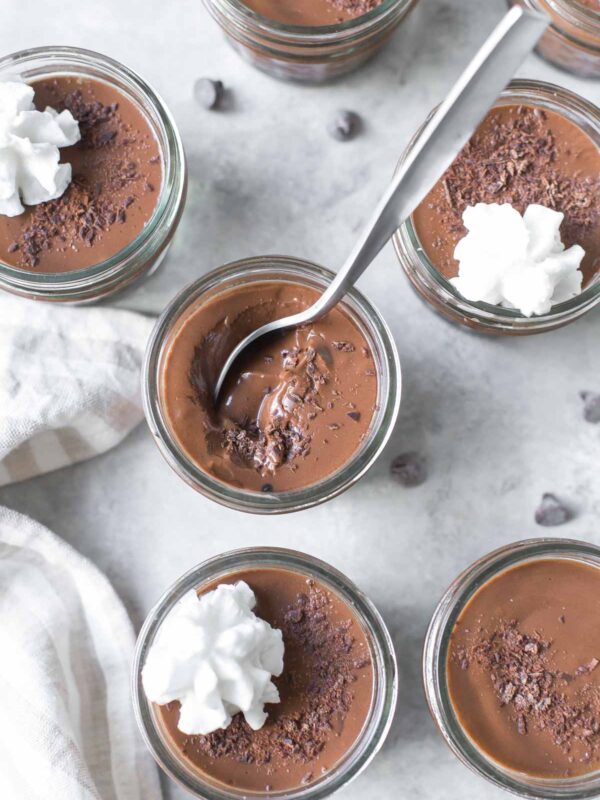 homemade chocolate pudding in small mason jars topped with chocolate shavings and dairy free whipped cream on a gray surface