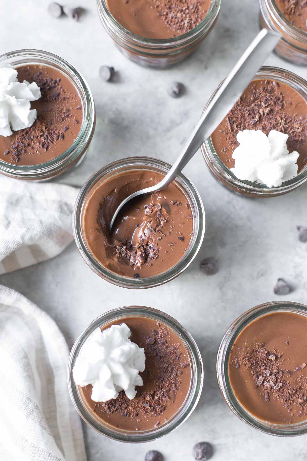 homemade chocolate pudding in small mason jars topped with chocolate shavings and dairy free whipped cream on a gray surface