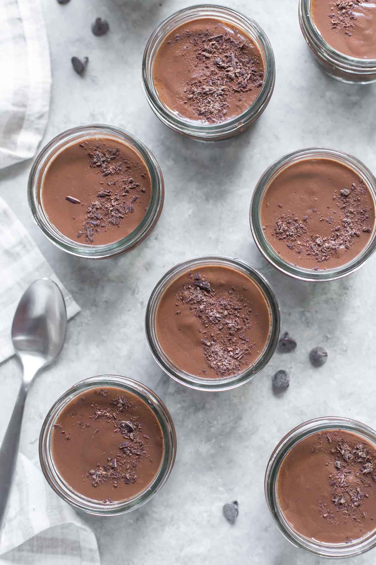 overhead view of closeup of a homemade chocolate pudding recipe in small mason jars topped with chocolate shavings on a gray surface