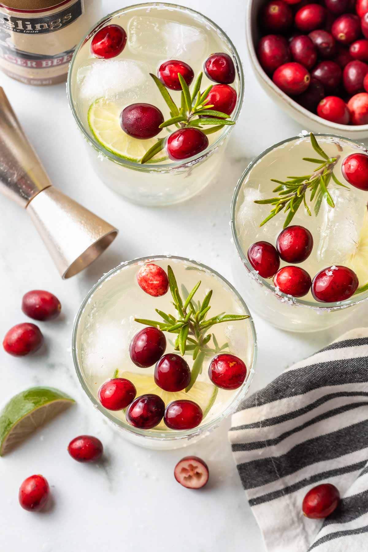 overhead view of three glasses with white christmas margarita garnished with cranberries, lime slice, and rosemary