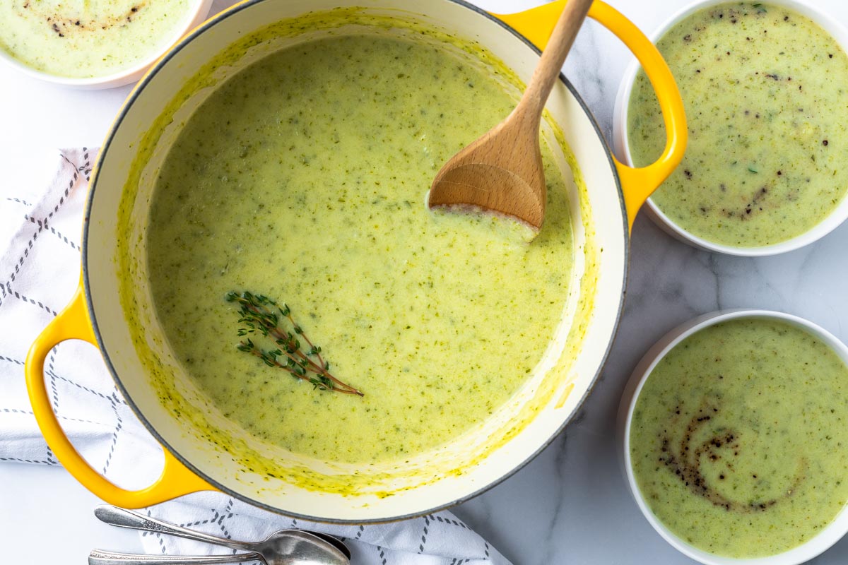 overhead view of zucchini soup in a yellow dutch over with a wooden spoon