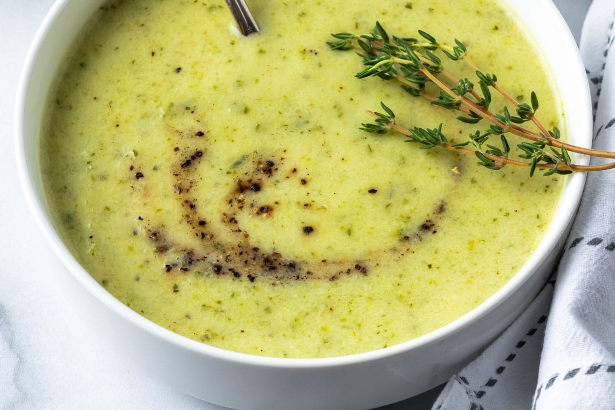 close up view of creamy zucchini soup with garnish is a small white bowl