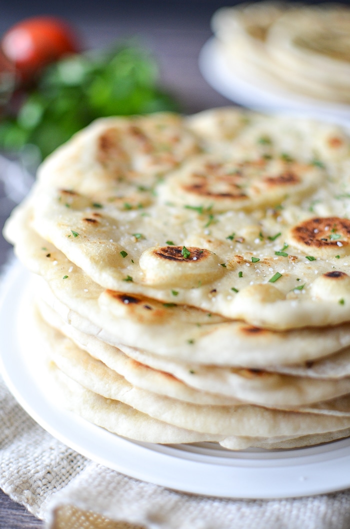 garlic naan bread stacked on a plate and sprinkled with fresh herbs