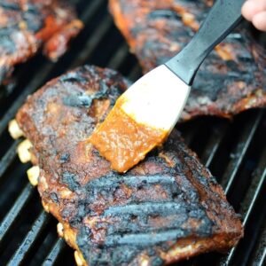 A basting brush brushing bbq sauce onto ribs on a grill.