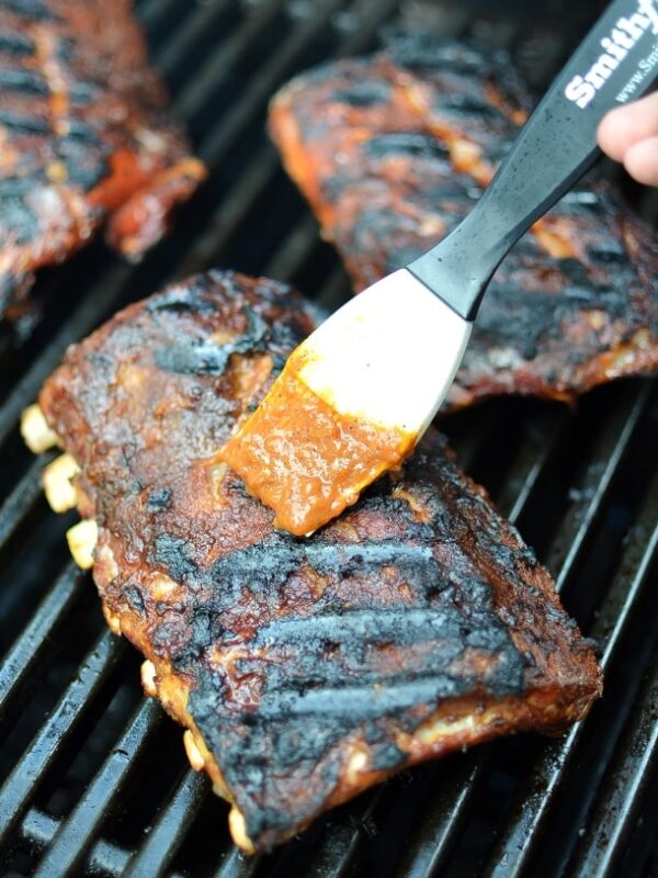 A basting brush brushing bbq sauce onto ribs on a grill.