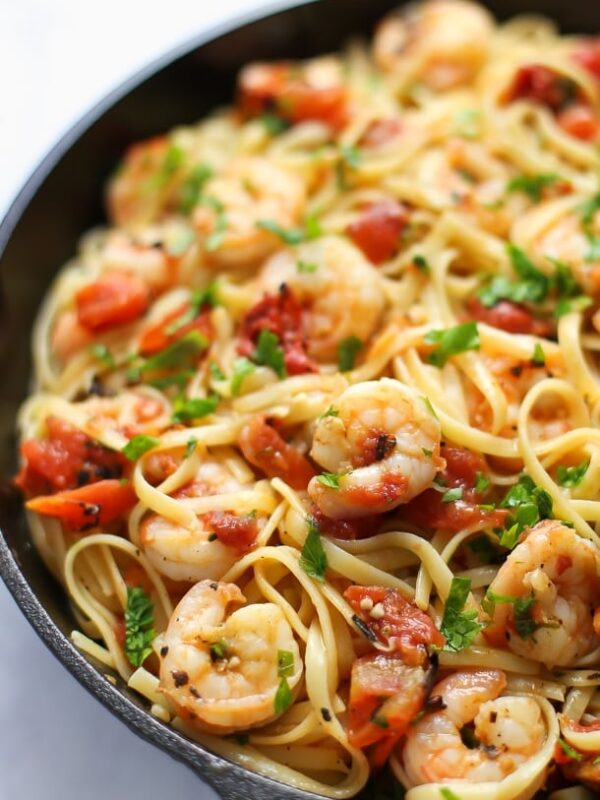 A skillet filled with shrimp fettuccine, diced tomatoes, and fresh herbs, all tossed together and garnished with chopped parsley.