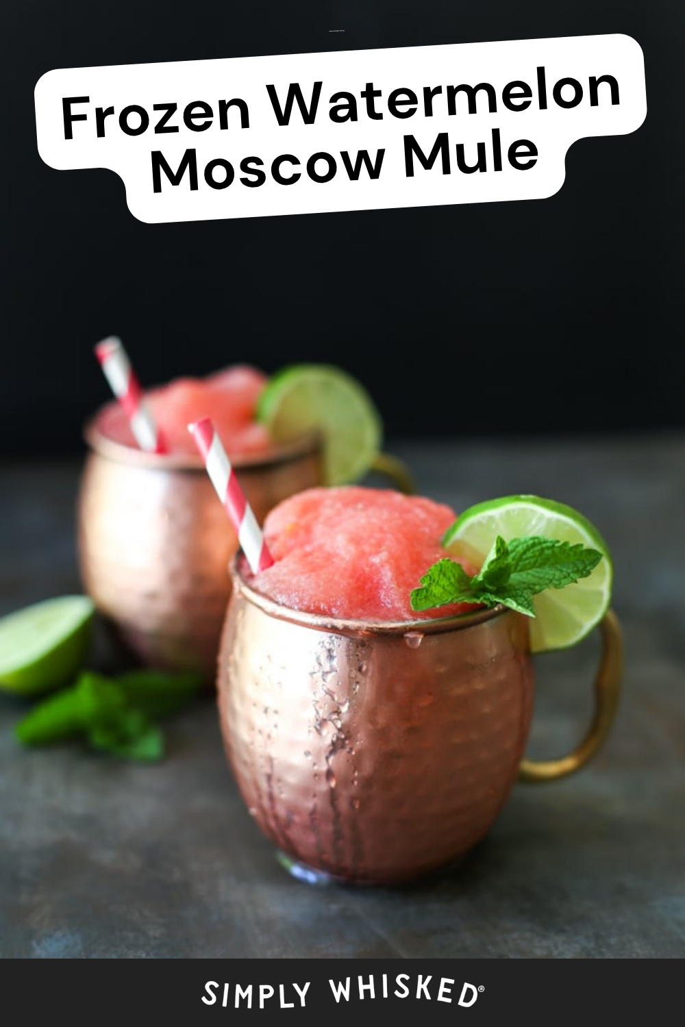 Two copper mugs filled with bright pink frozen watermelon Moscow mule, garnished with lime slices and mint, each with a striped straw. Two lime wedges and fresh mint are on the black surface nearby, completing this refreshing take on the classic frozen watermelon moscow mule cocktail.