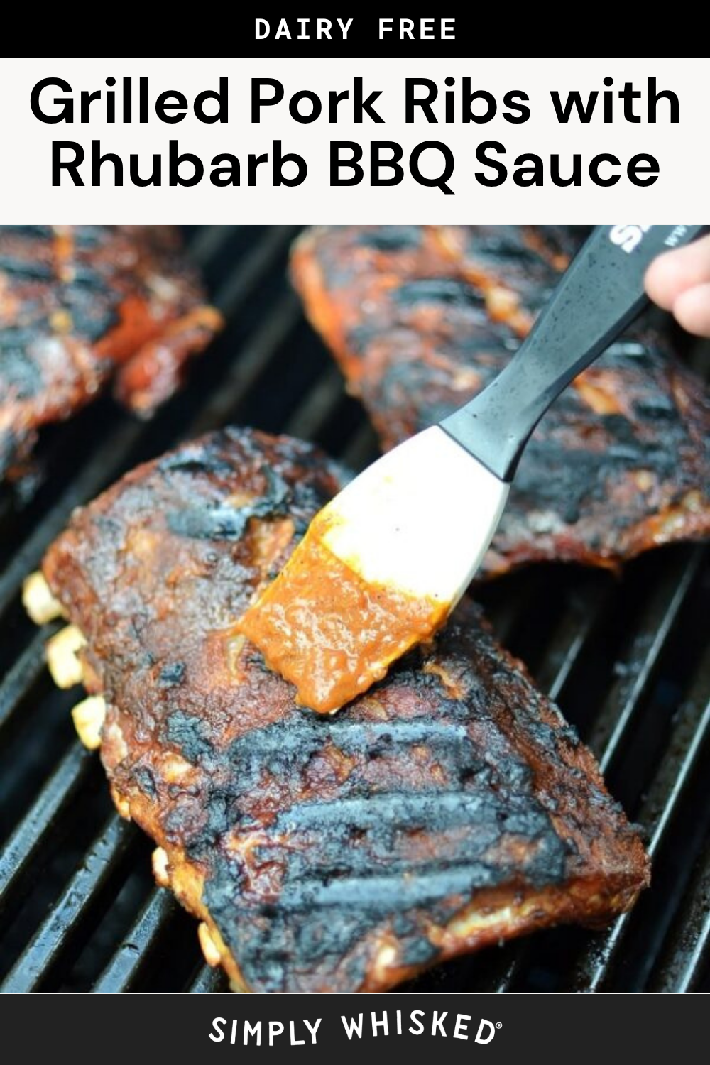 A hand brushes tangy rhubarb BBQ sauce onto grilled pork ribs on a barbecue grill. The ribs have grill marks and a caramelized coating.