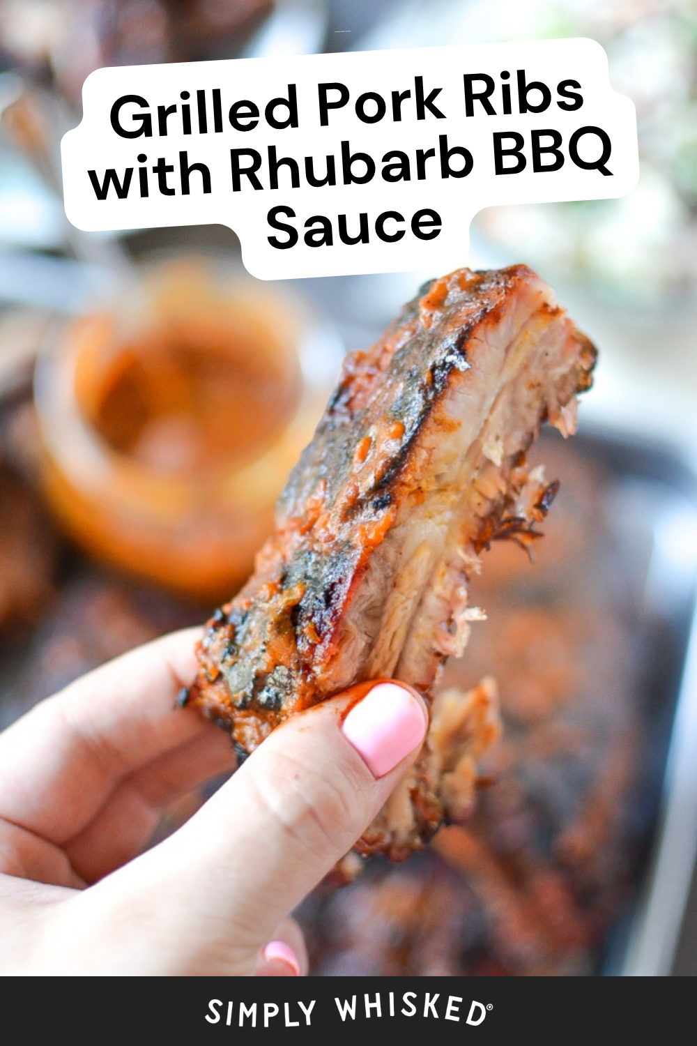 A hand with pink nail polish holds a grilled pork rib glazed with rhubarb BBQ sauce. Text reads Grilled Pork Ribs with Rhubarb BBQ Sauce. A tray of ribs and a bowl of tangy rhubarb BBQ sauce appear blurred in the background.