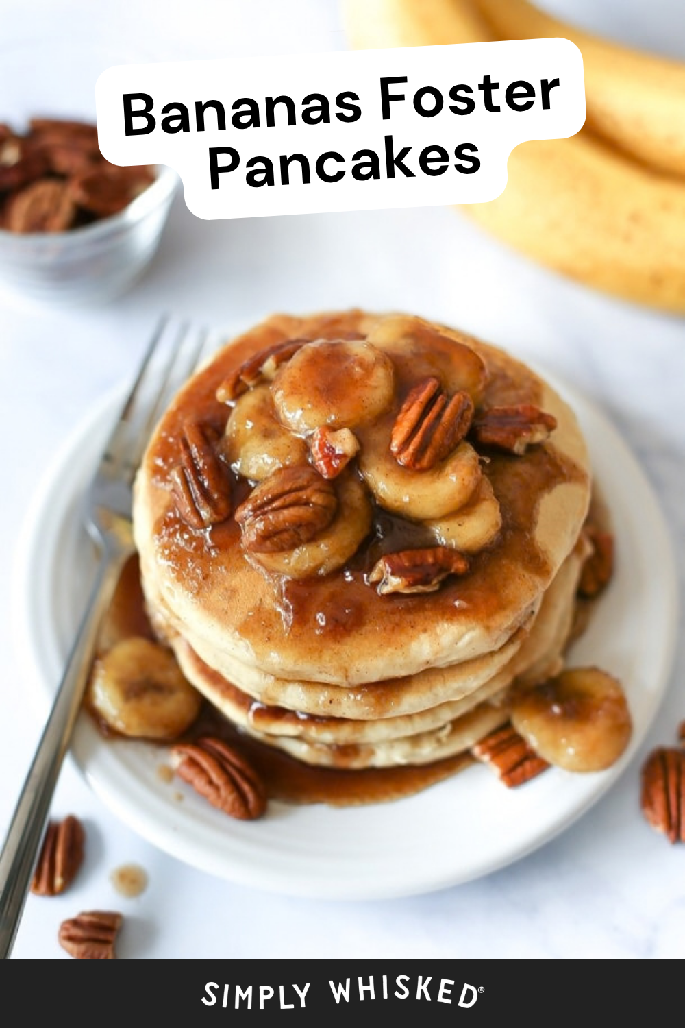 A stack of bananas foster pancakes topped with caramelized bananas, pecans, and syrup sits on a white plate, with a fork, scattered pecans, and bananas in the background. Text reads Bananas Foster Pancakes.