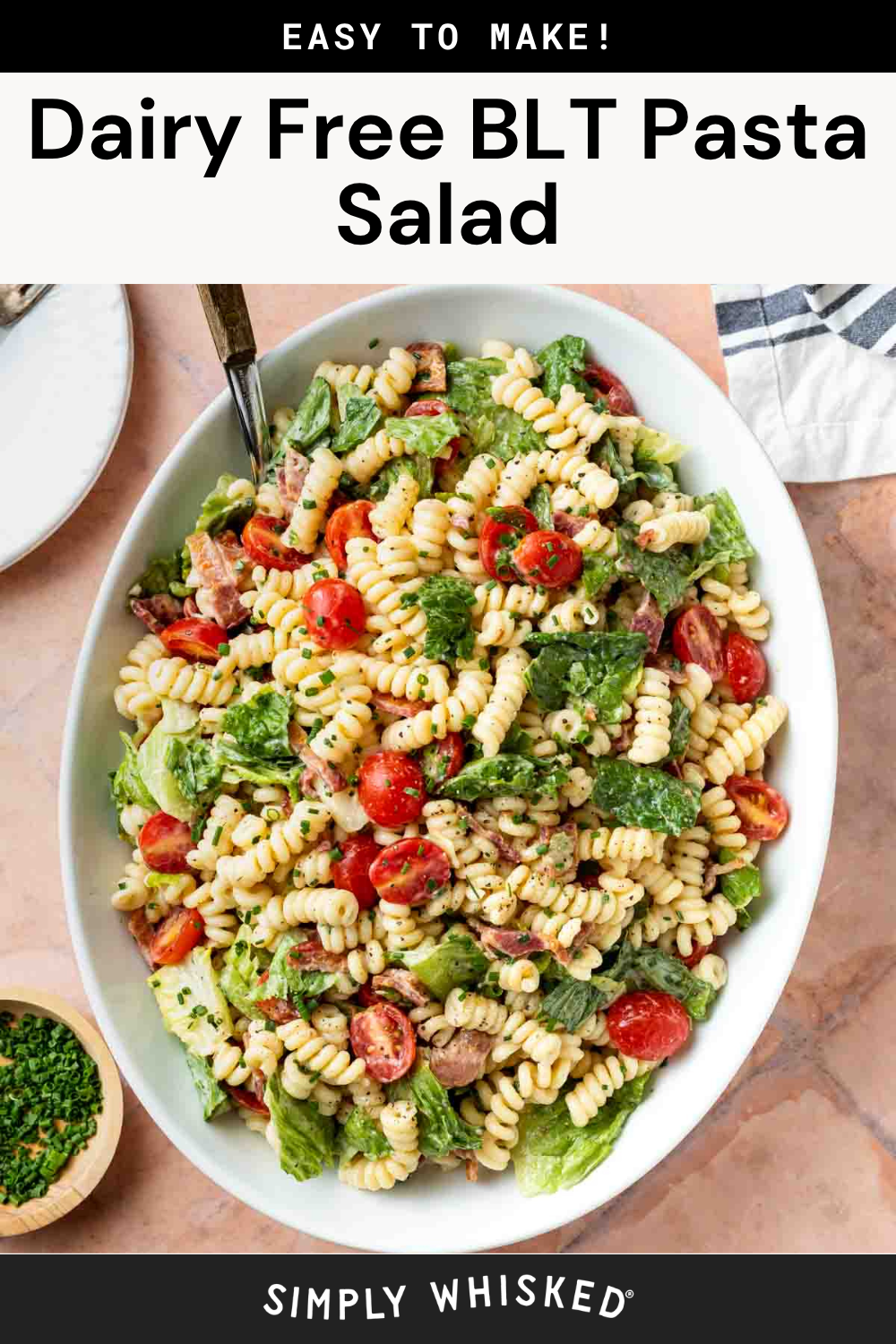 Oval platter of BLT pasta salad featuring rotini pasta, crisp lettuce, juicy cherry tomatoes, and savory bacon pieces on a light surface, garnished with fresh herbs. A small bowl of chopped herbs and a plate are nearby. Text reads: Dairy Free BLT Pasta Salad.