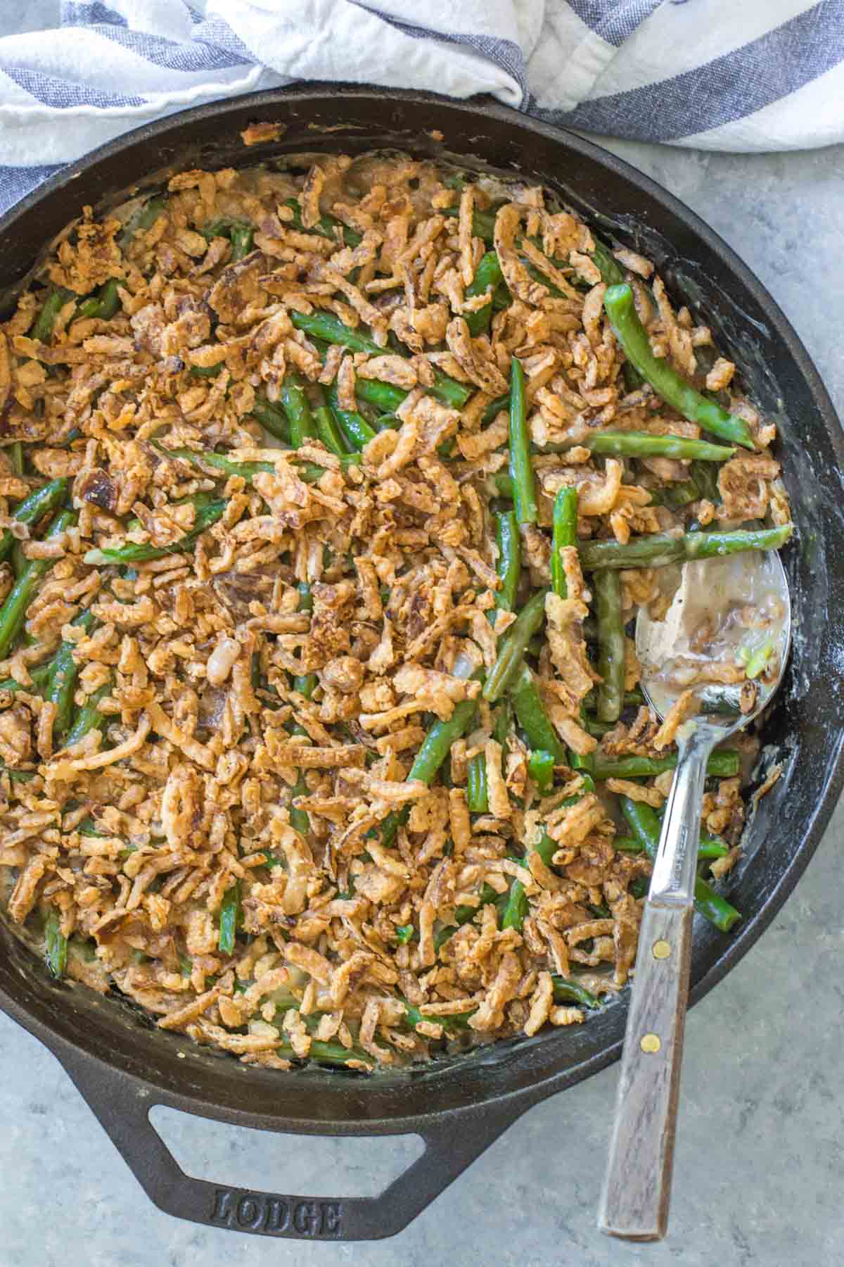 overhead shot, close up of cast iron skillet with dairy free green bean casserole with a serving spoon with wooden handle