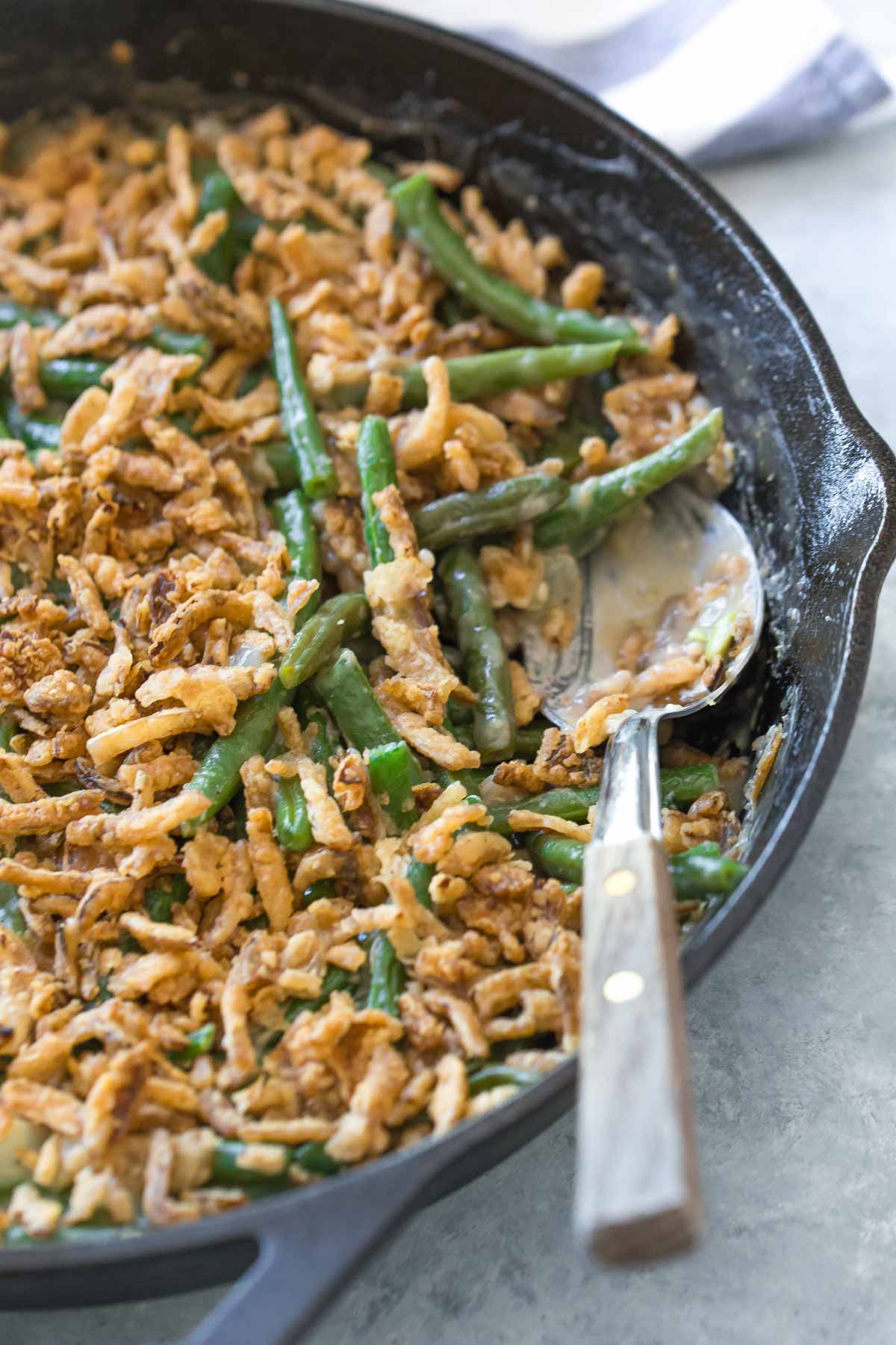 cast iron skillet with dairy free green bean casserole with a serving spoon with wooden handle