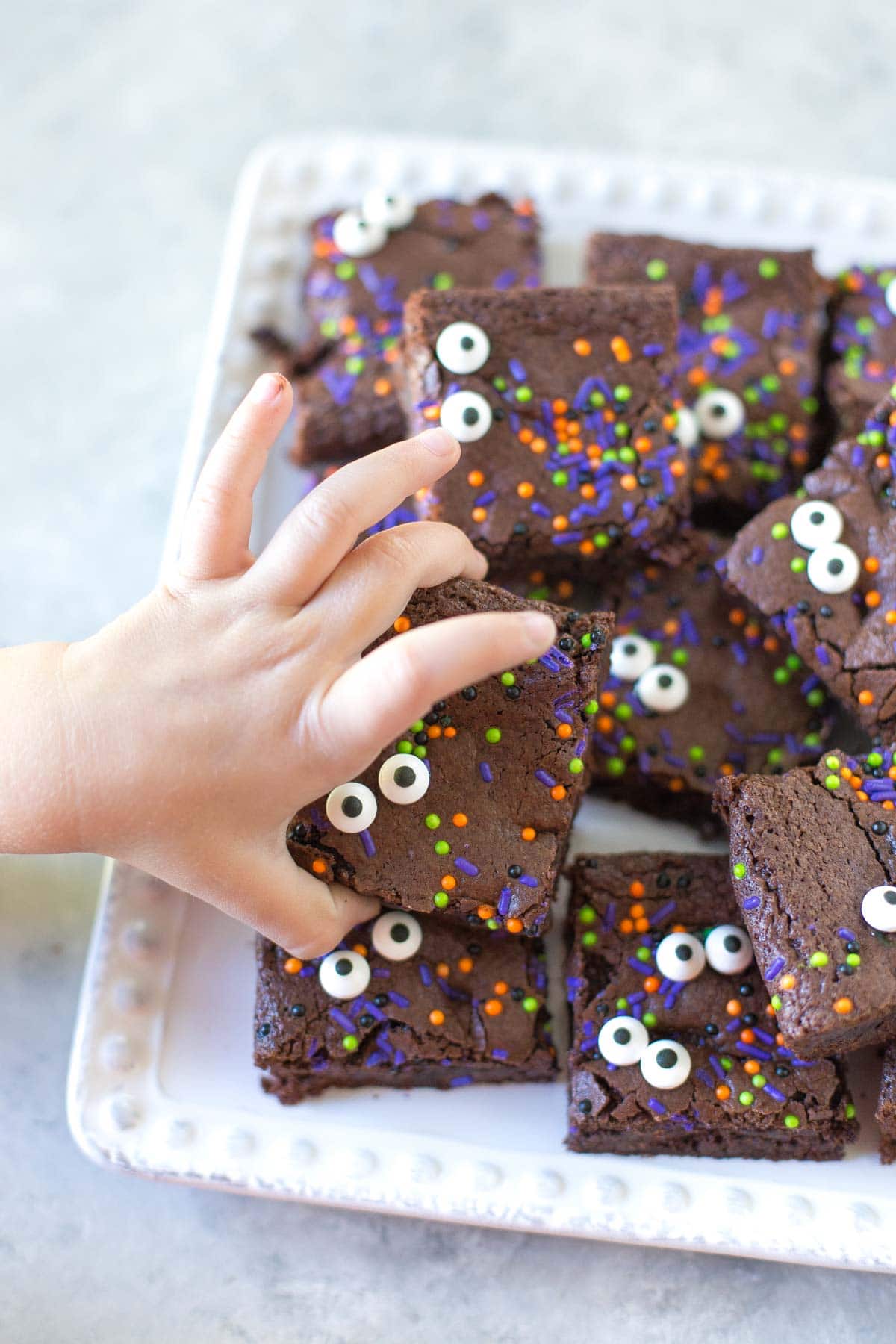 close up of plate of brownies with kids hand grabbing a spooky eyed brownie