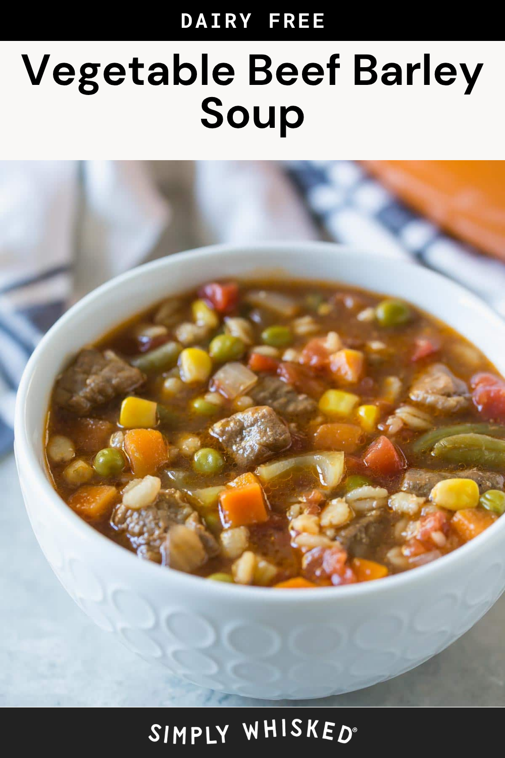 A white bowl filled with hearty beef barley soup, featuring tender beef chunks, barley, carrots, peas, corn, and green beans in a flavorful tomato-based broth, set on a light surface with a napkin in the background.