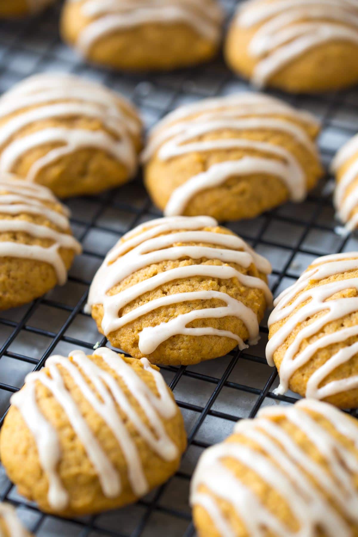 side close up of soft pumpkin cookies drizzled with cinnamon glaze on a cooling rack
