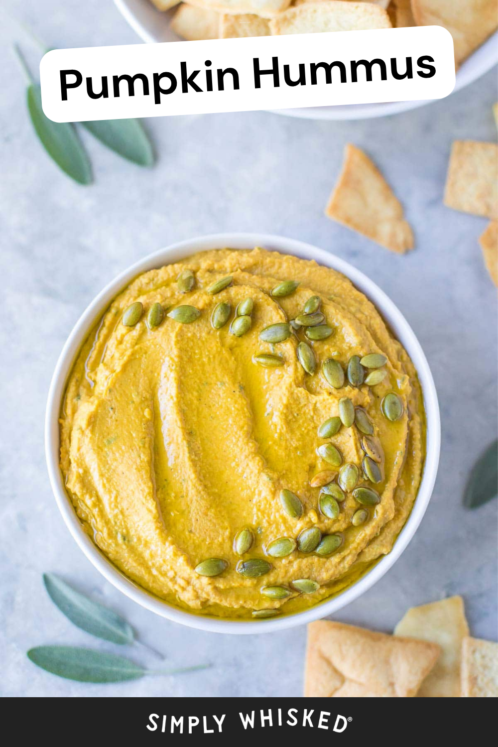 A white bowl of pumpkin hummus topped with pumpkin seeds, surrounded by pita chips and sage leaves on a light surface. The creamy roasted garlic pumpkin hummus is accented with savory flavors, while Pumpkin Hummus and Simply Whisked text appears on the image.