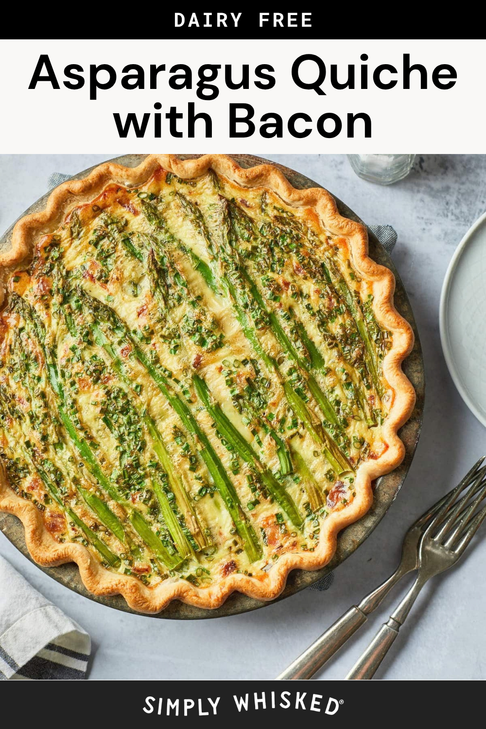A golden-brown asparagus quiche with bacon sits on a round plate, garnished with fresh green asparagus spears. A fork, knife, plate, and napkin are nearby. Text above reads Dairy Free Asparagus Quiche with Bacon.