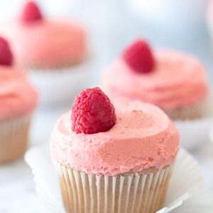 close up of raspberry cupcakes on a marble background with a bowl of raspberries in the background