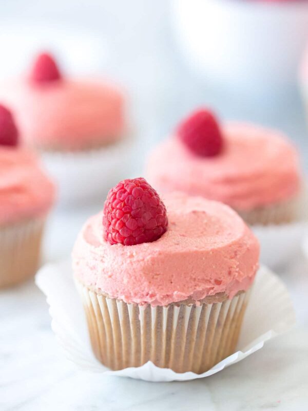 close up of raspberry cupcakes on a marble background with a bowl of raspberries in the background