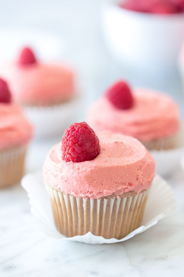 close up of raspberry cupcakes on a marble background with a bowl of raspberries in the background