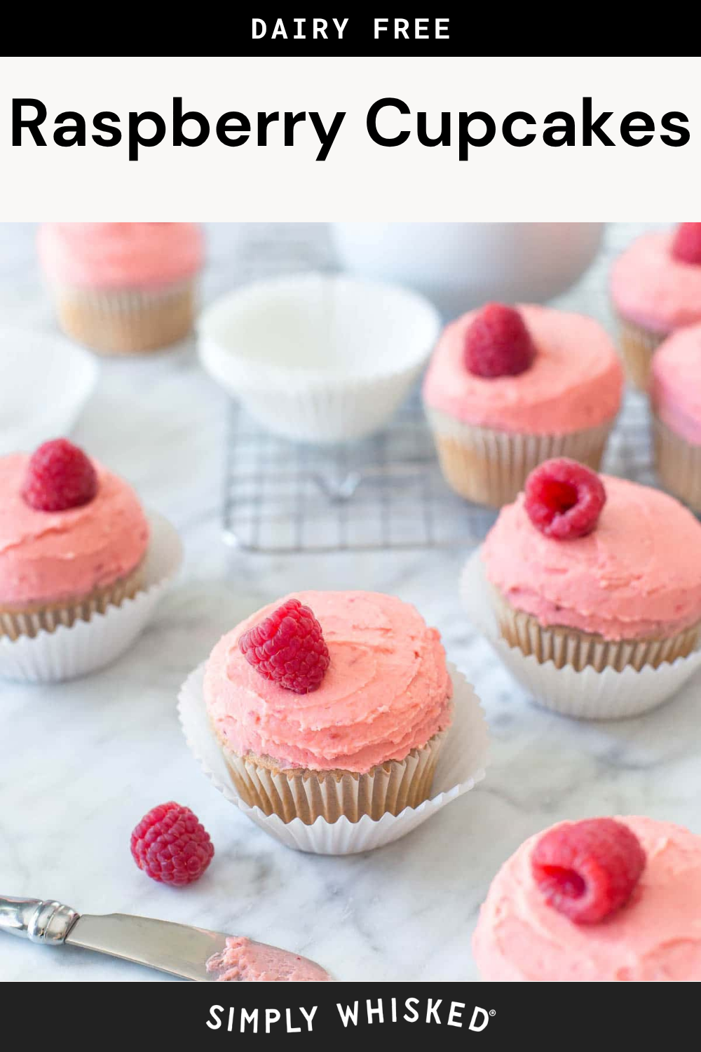 Dairy-free raspberry cupcakes with pink frosting and fresh raspberries on top, these delightful raspberry cupcakes are arranged on a marble surface with a wire cooling rack and a bowl in the background.