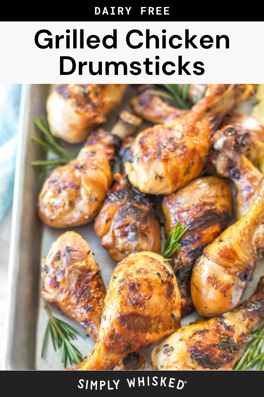 A tray of Grilled Chicken Drumsticks garnished with rosemary sits ready to serve. The drumsticks are golden brown and arranged closely together on a metal baking sheet.