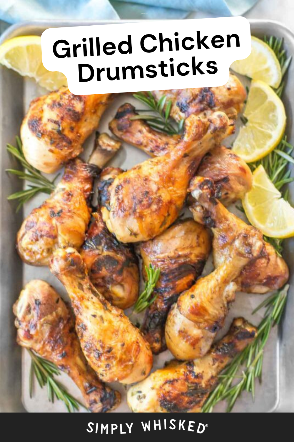 A tray of juicy Grilled Chicken Drumsticks, garnished with rosemary sprigs and lemon slices. The text Grilled Chicken Drumsticks is displayed at the top, and Simply Whisked at the bottom.