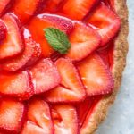 closeup of strawberry tart on a gray background with a small mint leaf on top