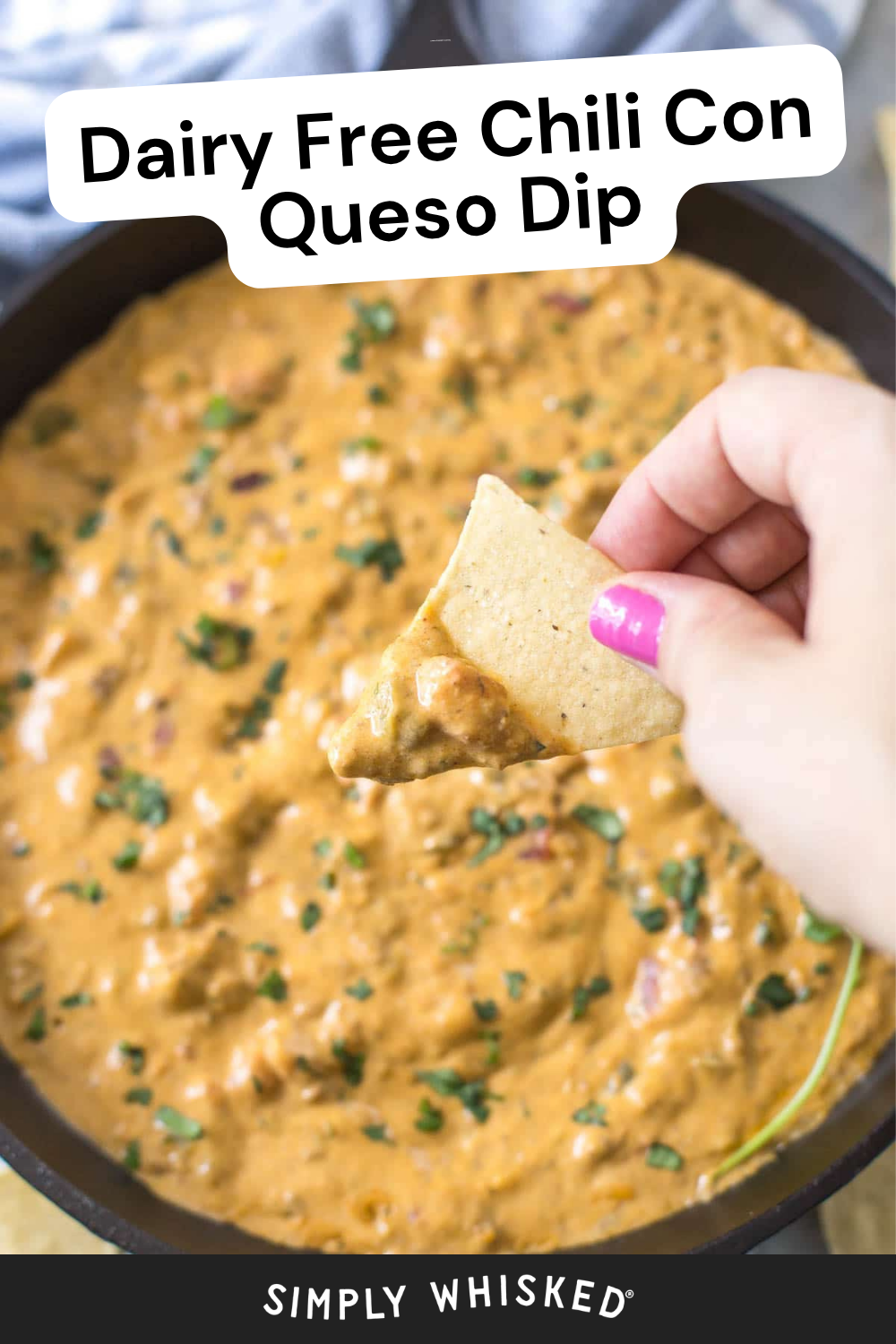 A hand with pink nail polish dips a tortilla chip into a skillet of creamy chili con queso dip, garnished with fresh herbs. Text on image says Dairy Free Chili Con Queso Dip.
