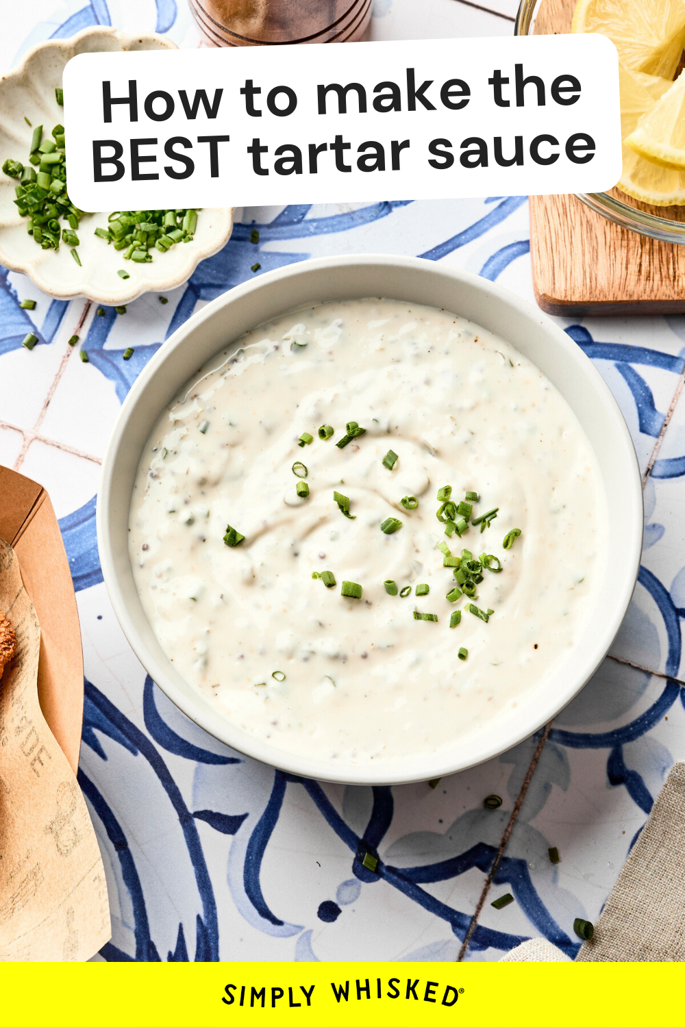 A bowl of homemade tartar sauce topped with chopped chives sits on a blue and white patterned surface. Nearby are lemon wedges, more chives, and a wooden spoon. Text reads, How to make the BEST tartar sauce recipe.