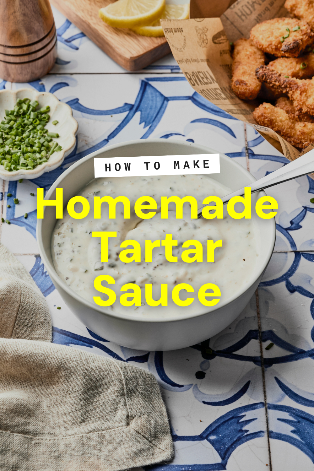 A bowl of creamy homemade tartar sauce with herbs sits on a blue and white tile surface, surrounded by chopped chives, lemon wedges, fried food, and a napkin. Text reads: How to Make the Best Tartar Sauce Recipe.