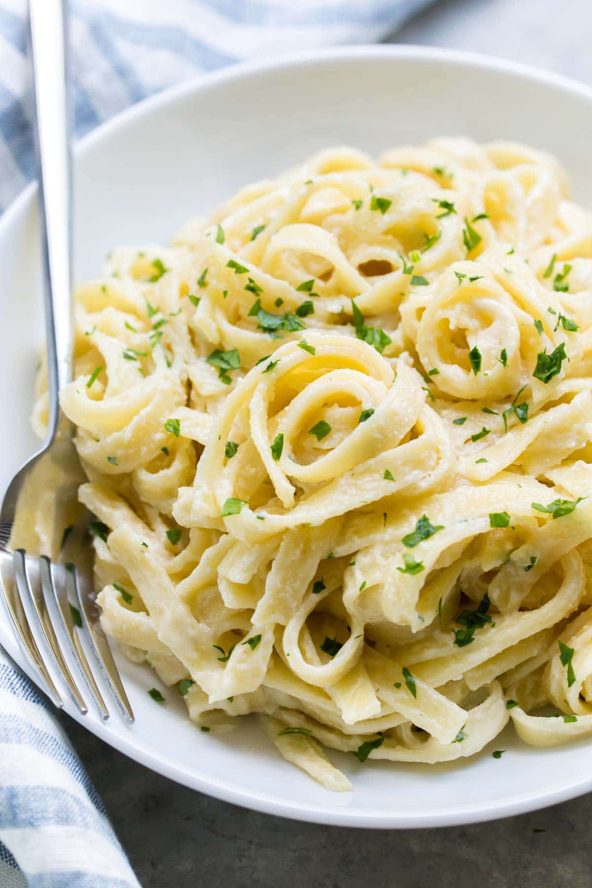 close up of dairy free alfredo sauce on fettuccini in a white bowl topped with chopped parsley
