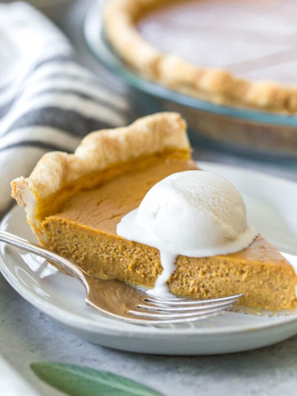closeup of a slice of dairy free pumpkin pie topped with a scoop of melting dairy free vanilla ice cream