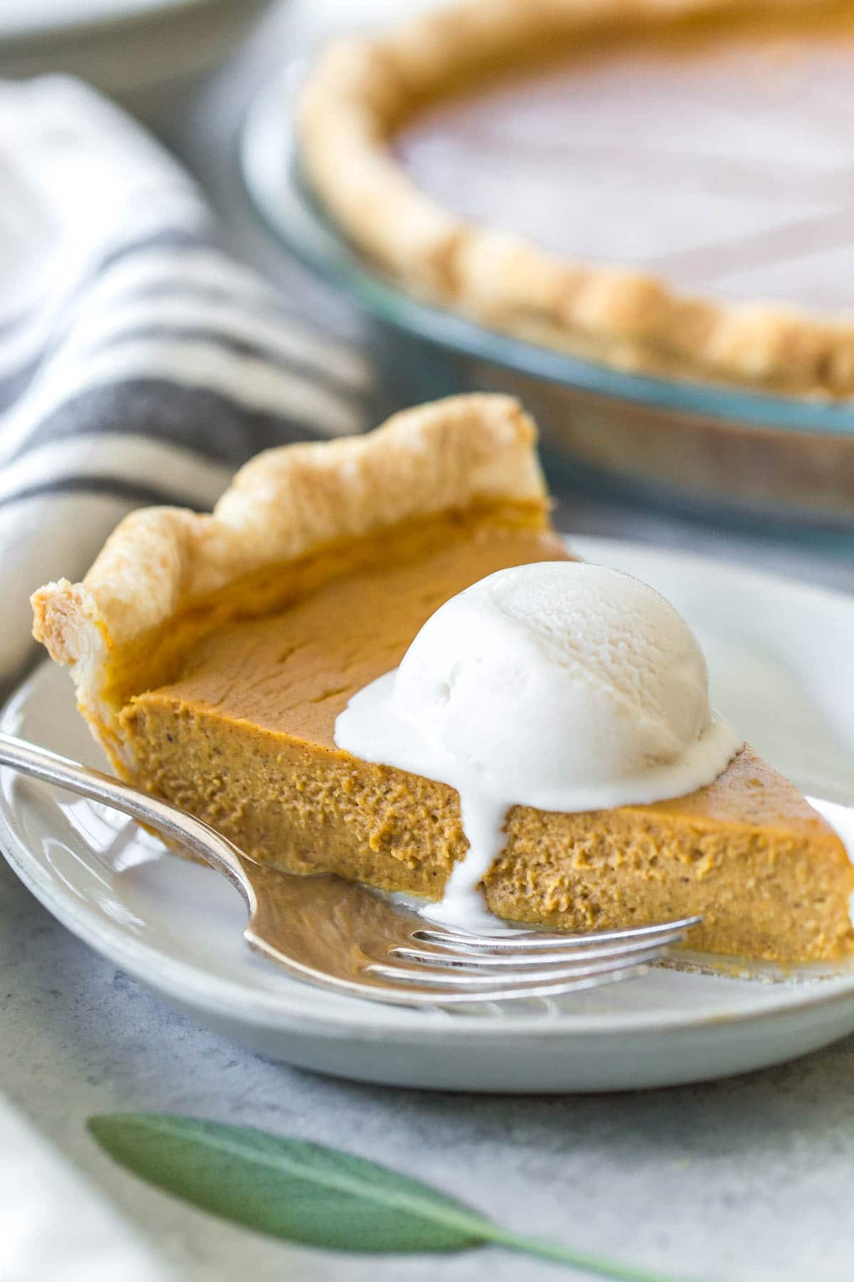 closeup of a slice of dairy free pumpkin pie topped with a scoop of melting dairy free vanilla ice cream
