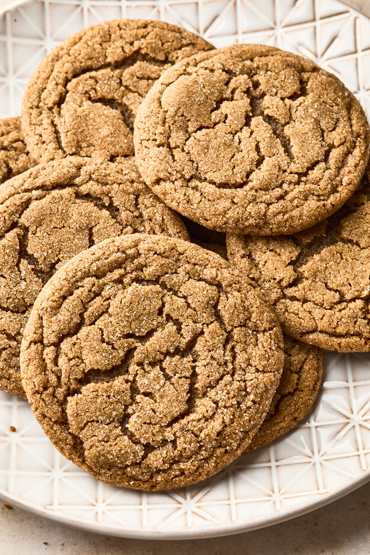 A plate of golden brown, cracked-top soft gingersnap cookies arranged in a slightly overlapping pattern on a white, textured plate.