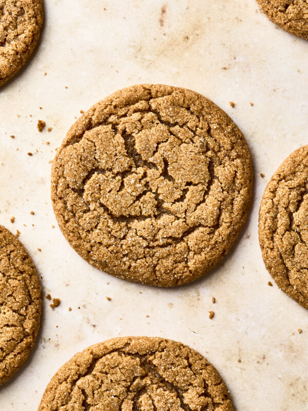 A close-up view of several round, golden-brown soft gingersnap cookies with a cracked surface, arranged on a light-colored baking sheet.