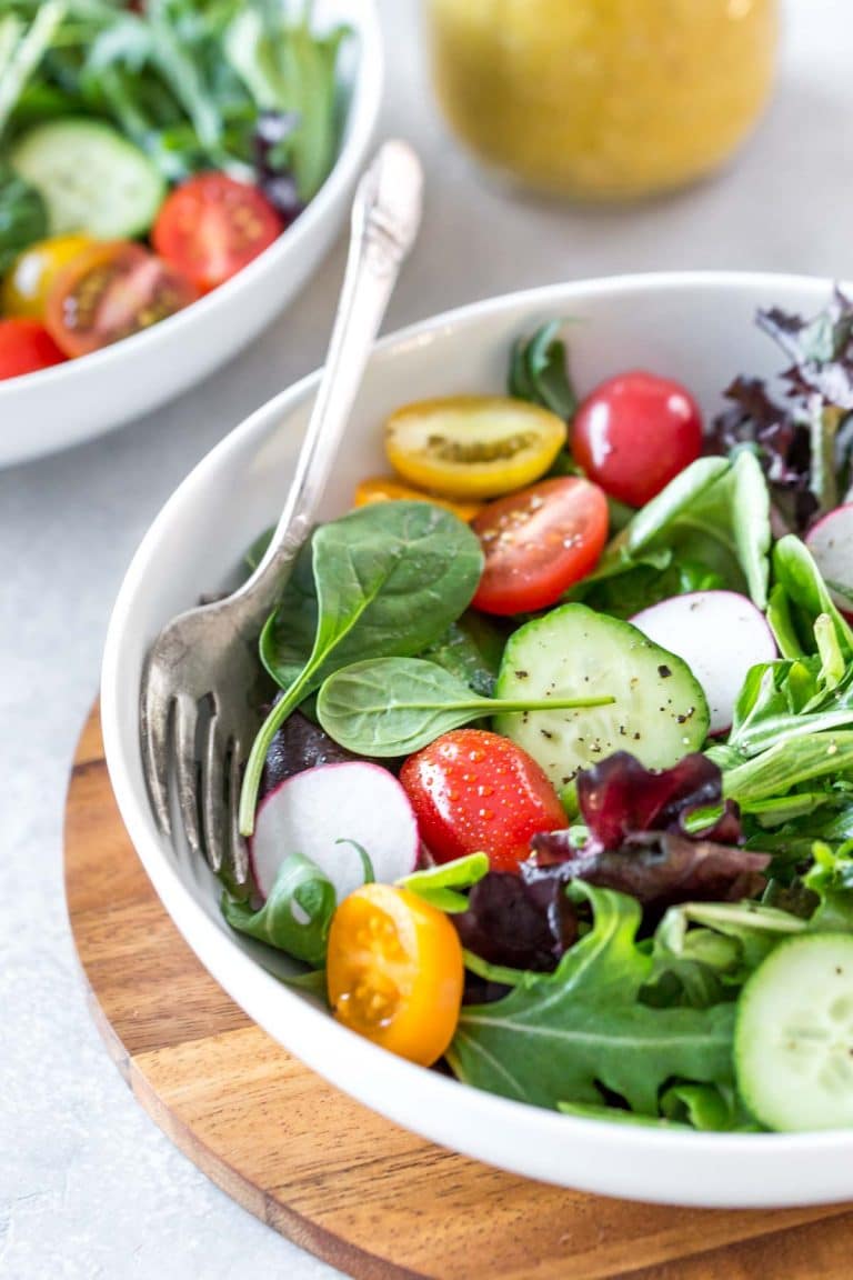 closeup of a colorful salad topped with Dijon vinaigrette with a fork on the side of a white bowl 
