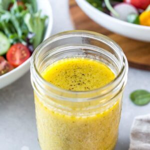 Easy Dijon vinaigrette in a mason jar with two salads in the background