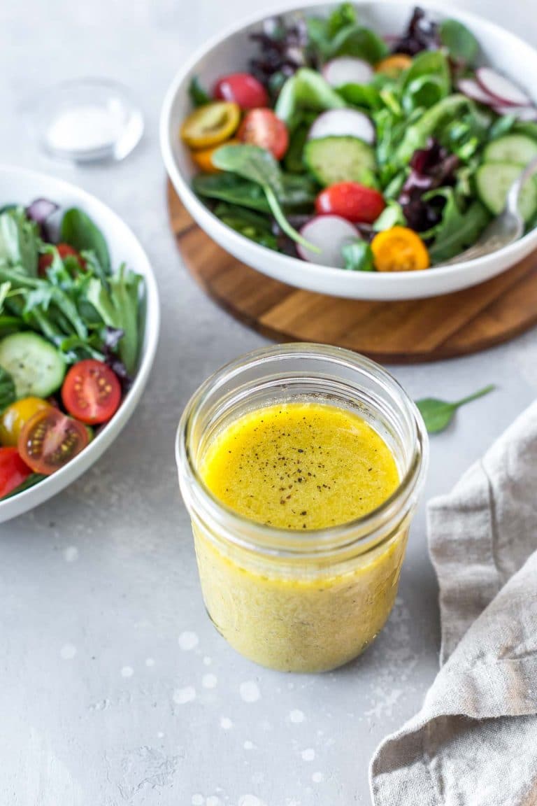 Easy Dijon vinaigrette in a mason jar with two salads in the background and a linen napkin to the side