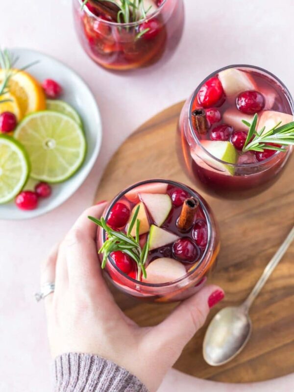 two glasses of christmas sangria, a hand taking one from a wooden tray