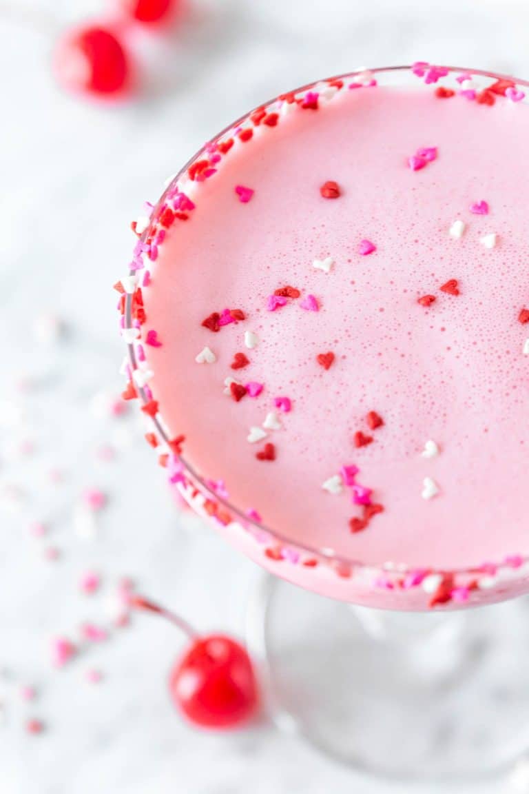 overhead shot of a pink squirrel cocktail in a coupe glass rimmed with miniature heart sprinkles and sprinkles floating on top