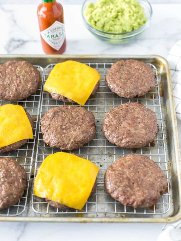 baked hamburgers on a cookie sheet with a cooling rack fitted inside