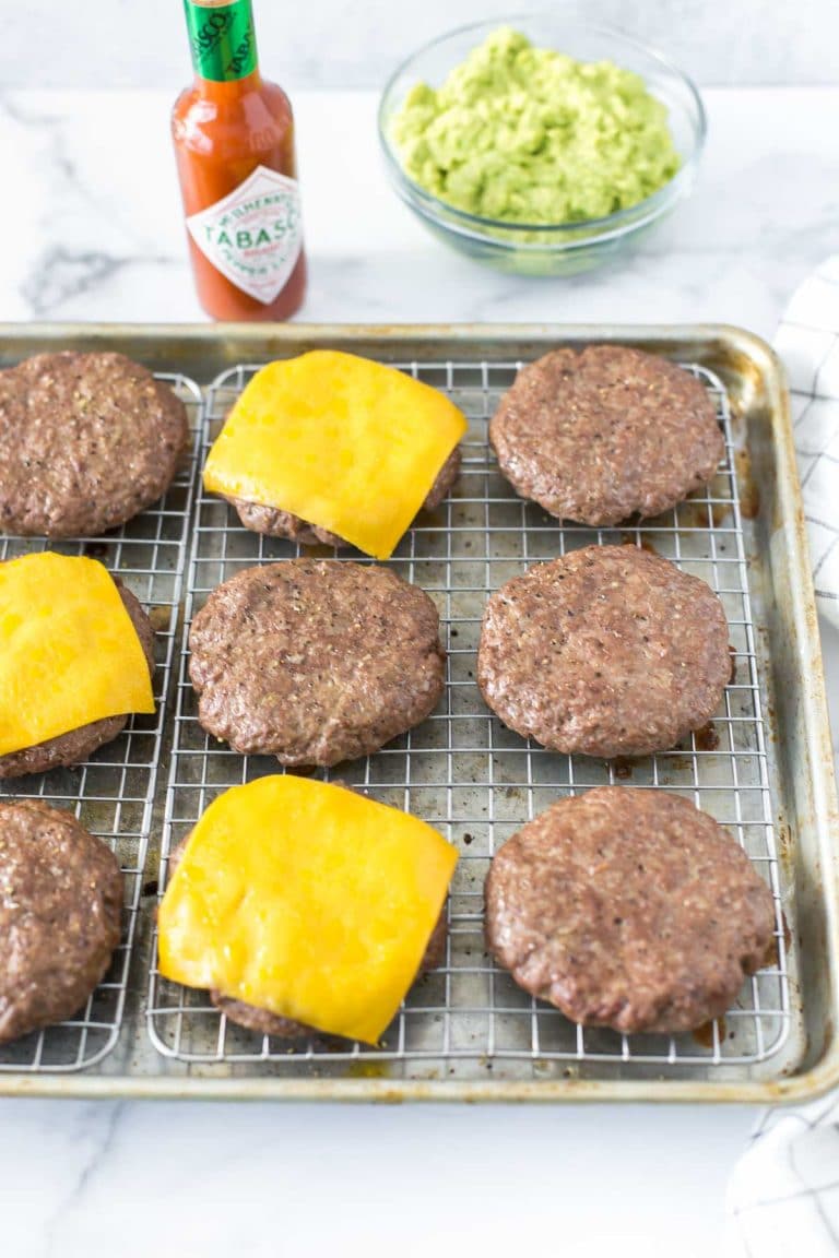 baked hamburgers on a cookie sheet with a cooling rack fitted inside